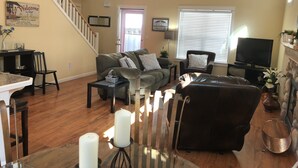 A living room with a staircase, a sofa, a TV, and a dining area with a table and chairs.