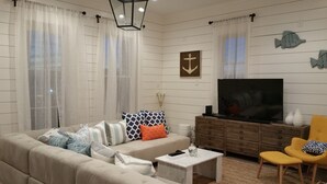 A living room with a sofa, coffee table, TV, and decorative fish wall art. - STUNNING! CUSTOM BEACH HOUSE, HOT TUB, BEACH JUST STEPS AWAY (Galveston)