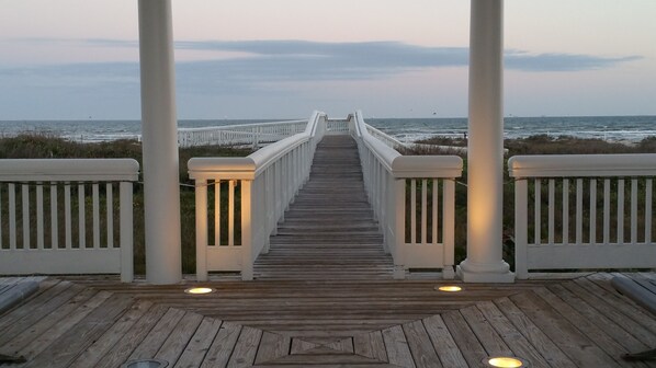 A wooden boardwalk leading to a white fence with railings, overlooking a beach and ocean. - STUNNING! CUSTOM BEACH HOUSE, HOT TUB, BEACH JUST STEPS AWAY (Galveston)