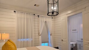 A hotel room with a large bed, a bedside lamp, a window with sheer curtains, and a view of the bathroom. - STUNNING! CUSTOM BEACH HOUSE, HOT TUB, BEACH JUST STEPS AWAY (Galveston)
