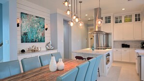 A modern kitchen with white cabinets, a wooden dining table, and blue chairs. - STUNNING! CUSTOM BEACH HOUSE, HOT TUB, BEACH JUST STEPS AWAY (Galveston)
