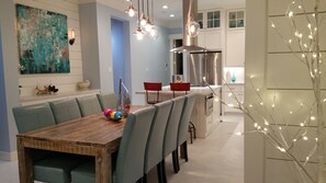 Un coin repas avec une table en bois, des chaises grises et un bol rempli de balles colorées. Des lampes suspendues sont placées au-dessus de la table, et un arbre décoratif illuminé se trouve à droite.