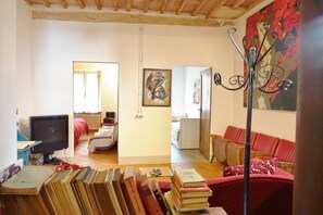 Un soggiorno con televisione, libri, un divano rosso e un quadro appeso al muro.