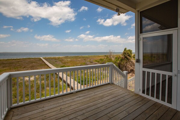 Une terrasse en bois avec une balustrade blanche, donnant sur une plage et l’océan.
