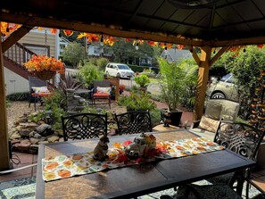 Un patio al aire libre con una mesa dispuesta para dos personas, rodeado de sillas y un mantel decorativo.
