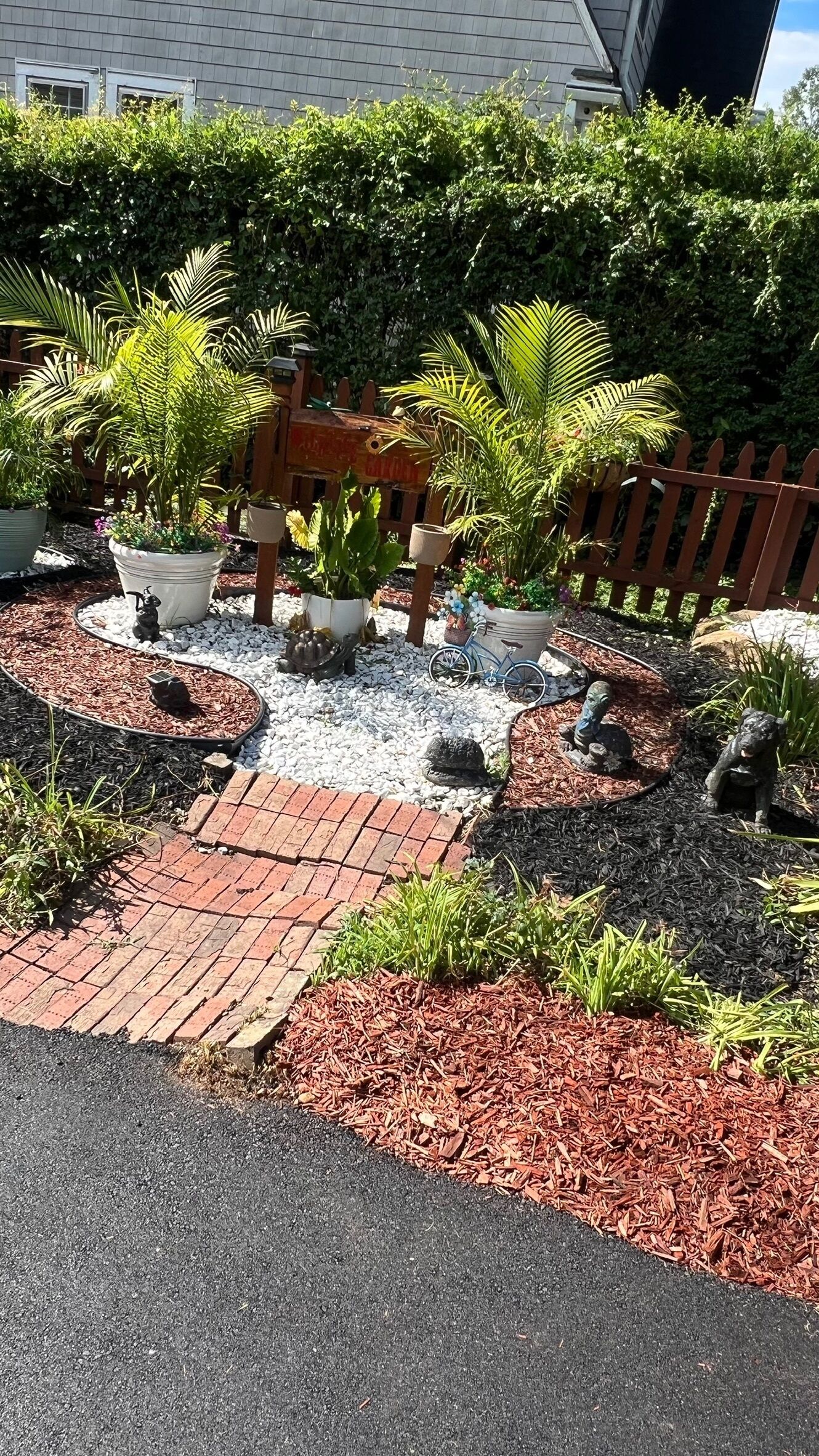 A garden with a brick pathway, mulch, decorative rocks, and potted plants.