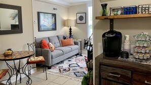A living room with a gray sofa, a coffee machine, and a tray of coffee cups.