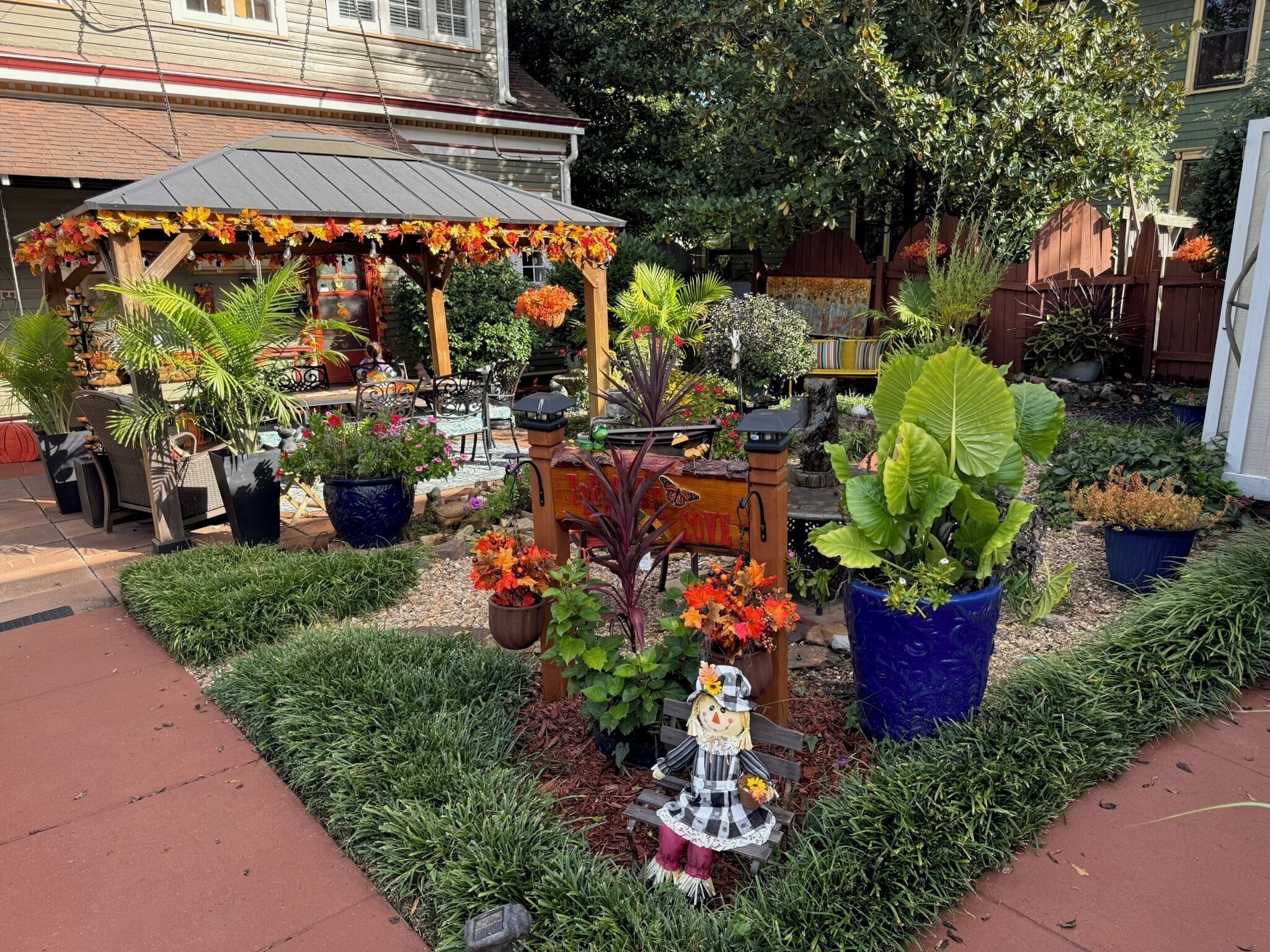 A garden with a gazebo, potted plants, and a scarecrow statue.