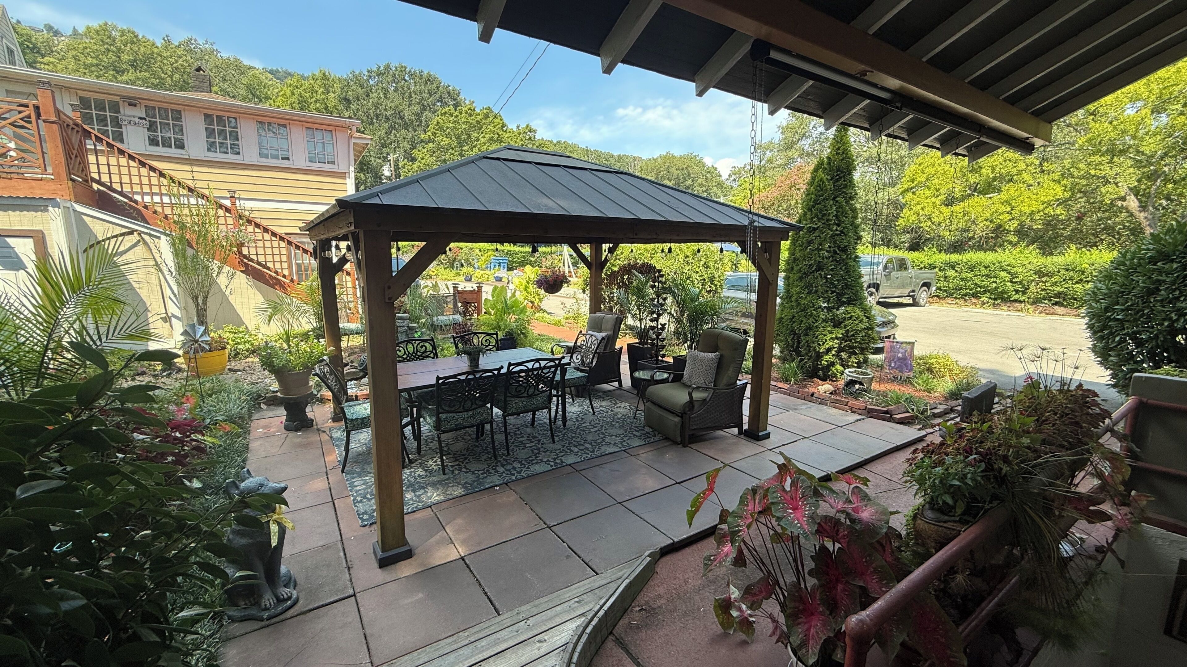 A covered patio area with a table and chairs, surrounded by potted plants and a pergola.