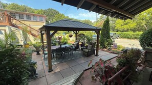 Un patio techado con mesa y sillas, rodeado de plantas en macetas y una pérgola.