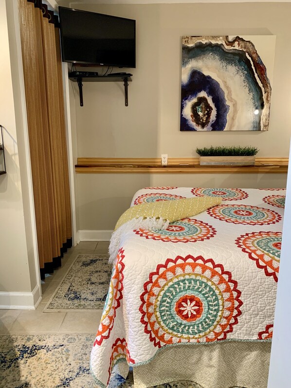Un dormitorio con cama, televisor, un cuadro y una planta pequeña.