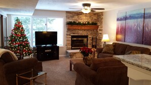 A living room with a stone fireplace, a Christmas tree, and a flat-screen TV. - Harbor Springs -Trout Creek Unit  84, spacious 1700, VERY CLEAN, Building 12 (Harbor Springs)