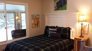 A bedroom with a bed, a window, a painting, and a lamp.