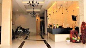 Un vestíbulo de hotel con una recepción, un candelabro y una motocicleta estacionada al fondo.