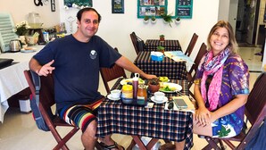 Un comedor con una mesa dispuesta para dos personas, que incluye un mantel a cuadros, una cafetera y diversos alimentos.