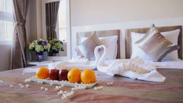 Una habitación de hotel con una cama bien hecha, una bandeja de fruta y un ramo de flores.