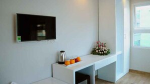 Una habitación moderna con un televisor de pantalla plana en la pared, una mesa blanca con cafetera y fruta, y una ventana con vistas.