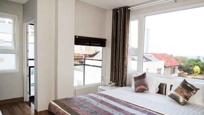 Un dormitorio con una cama grande, una ventana con cortinas y vistas a edificios.