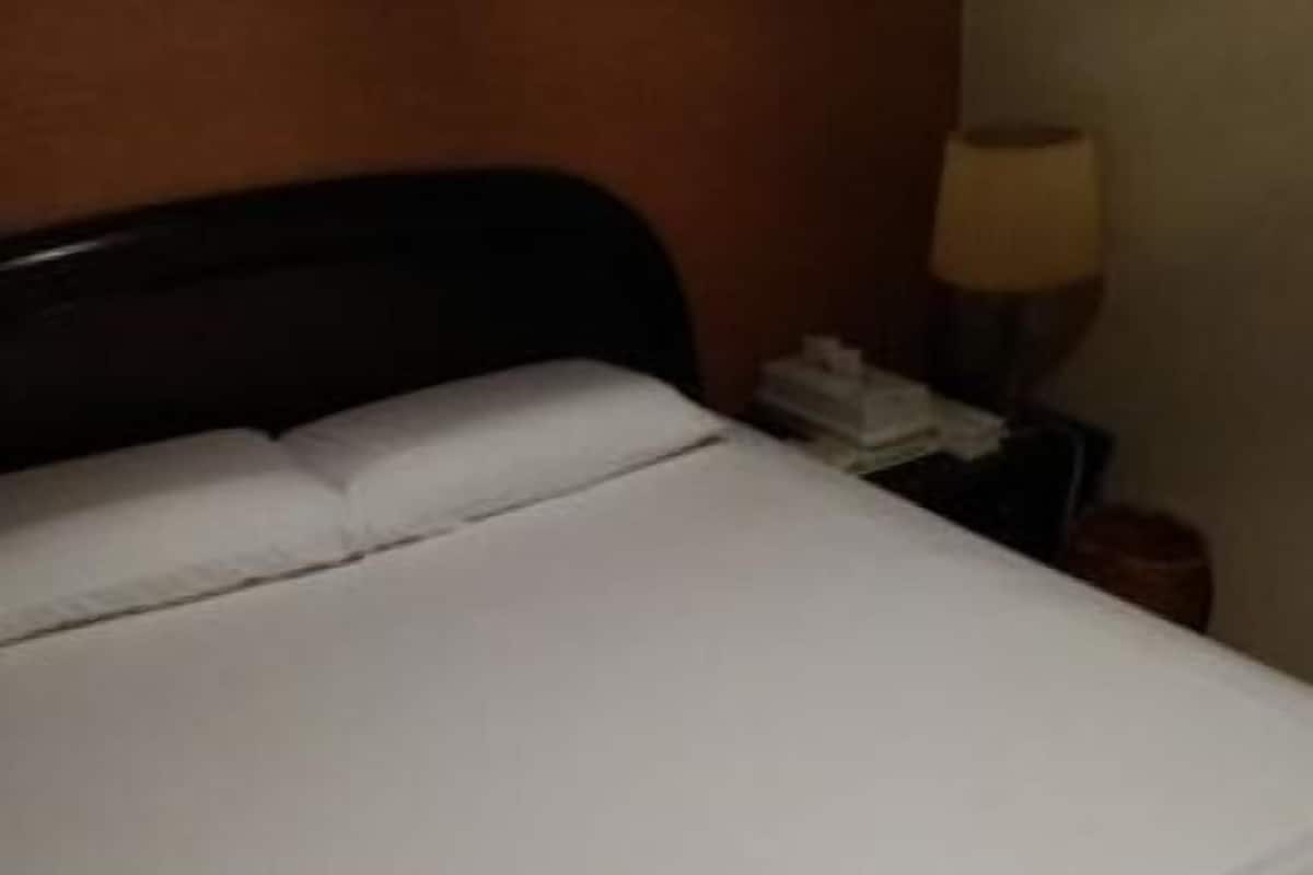 A bed with white bedding, a wooden headboard, and a nightstand with a lamp.