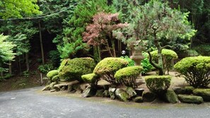 A pathway lined with neatly trimmed bushes and rocks, leading through a forested area with various trees and a stone lantern. - Hotel Kegon - Adults Only (Nagasaki)