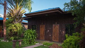A wooden house with two doors, surrounded by lush greenery and a palm tree. - Mountain View House (Sangkhla Buri)