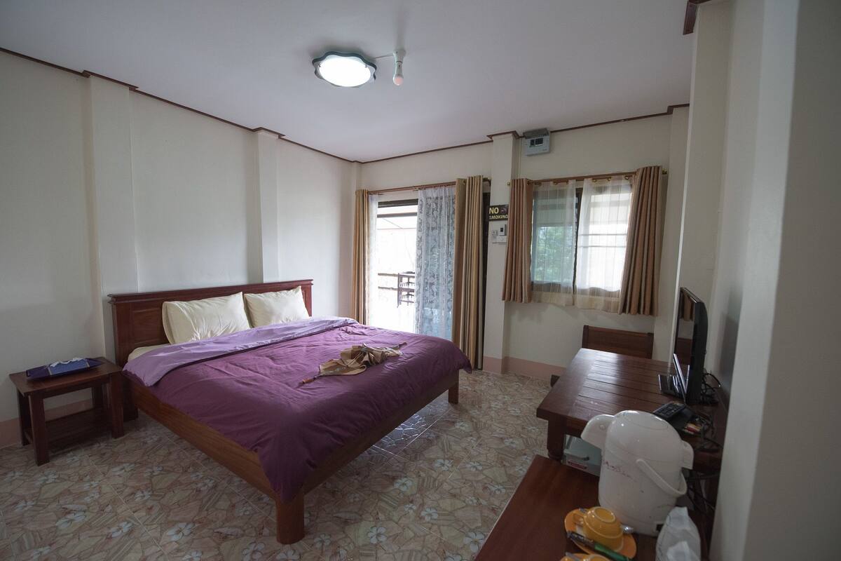 A bedroom with a bed, bedside table, desk, chair, and a television.