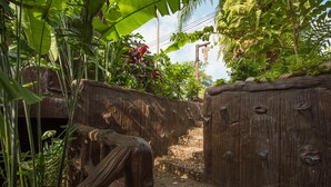 A narrow stone pathway flanked by wooden walls with carvings, surrounded by lush tropical vegetation. - Mountain View House (Sangkhla Buri)