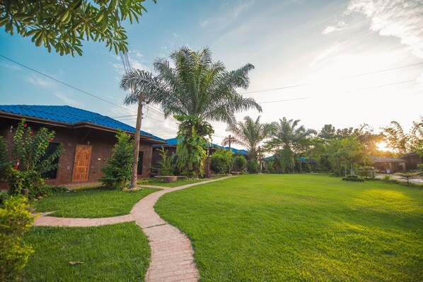 A pathway leading to a building with a blue roof, surrounded by lush greenery and palm trees.