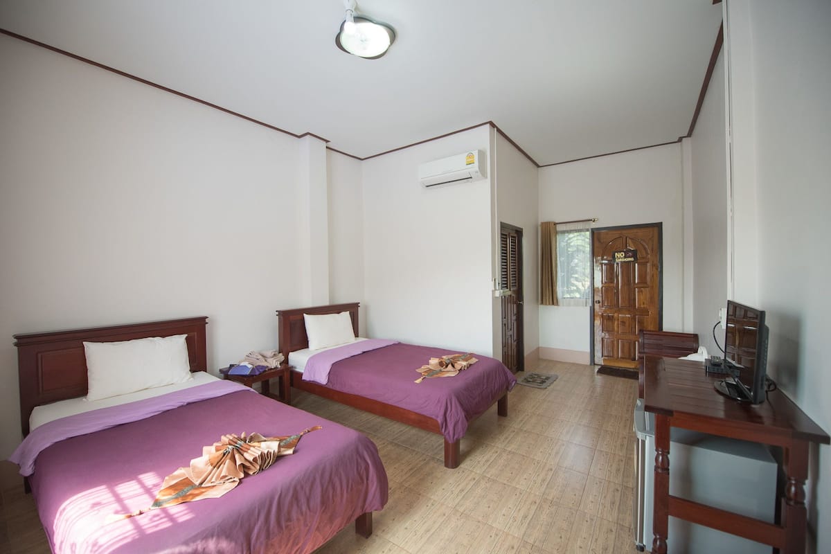 A hotel room with two beds, a desk, a television, and an air conditioning unit.