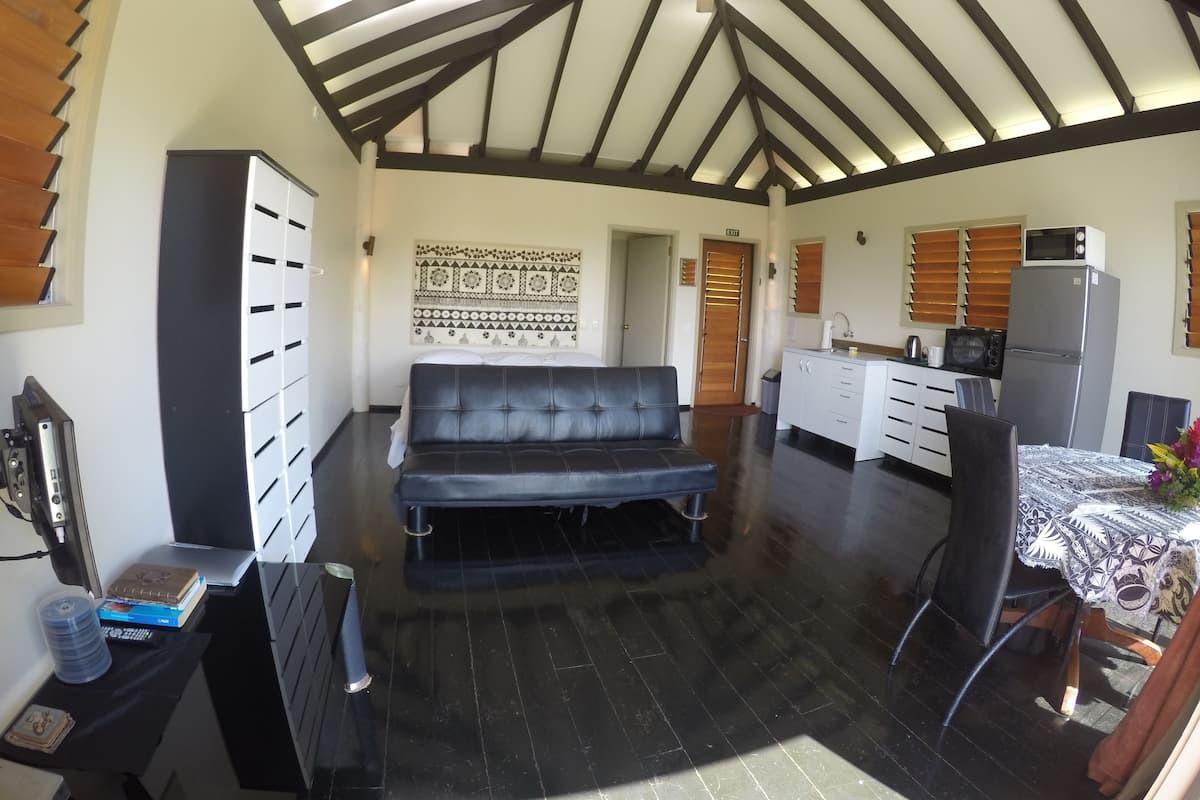 Un espacio habitable compacto con kitchenette, sofá, comedor y techo con vigas a la vista.
