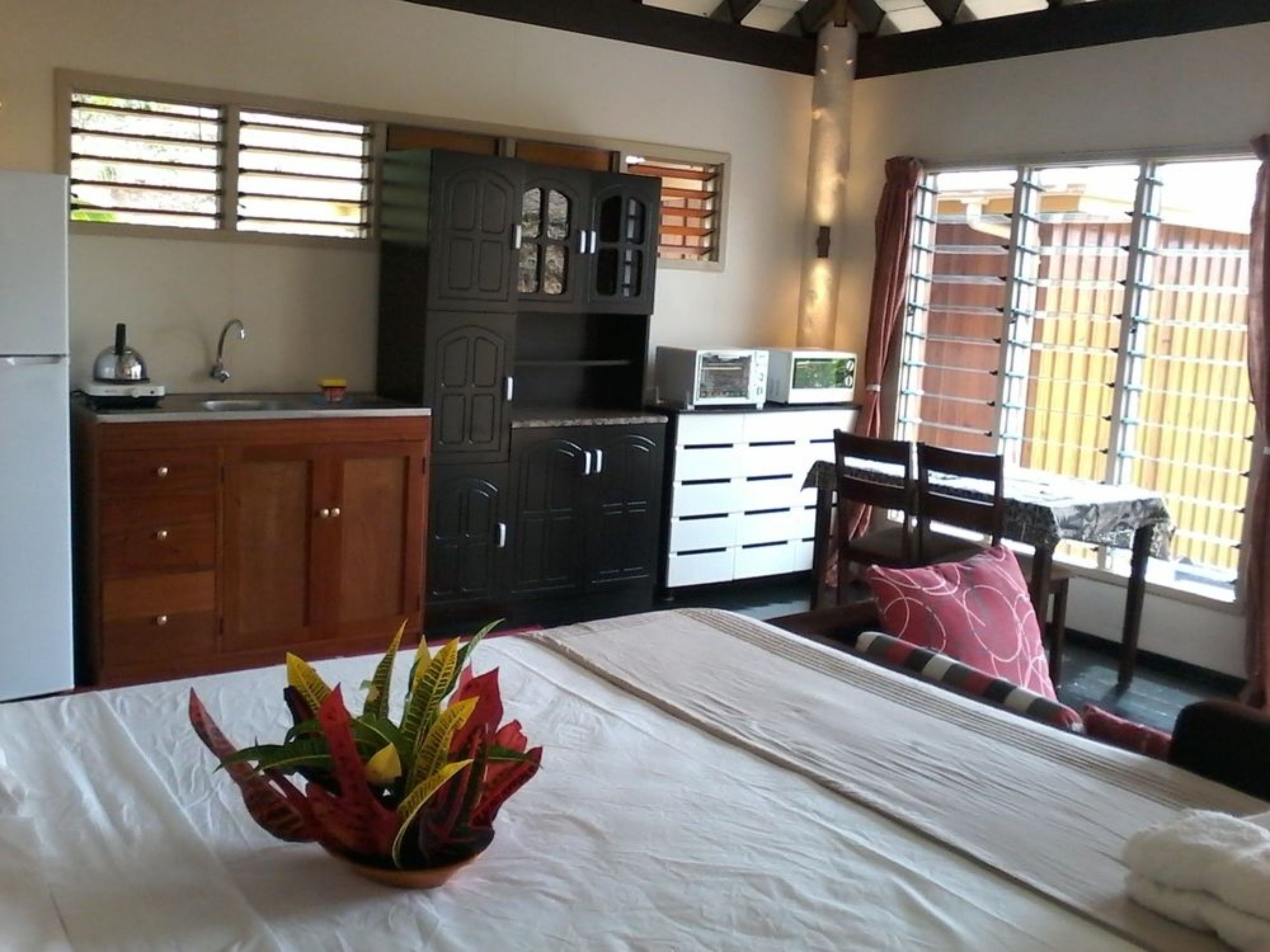 A compact room with a bed, a small kitchenette, a dining area, and a window with blinds.
