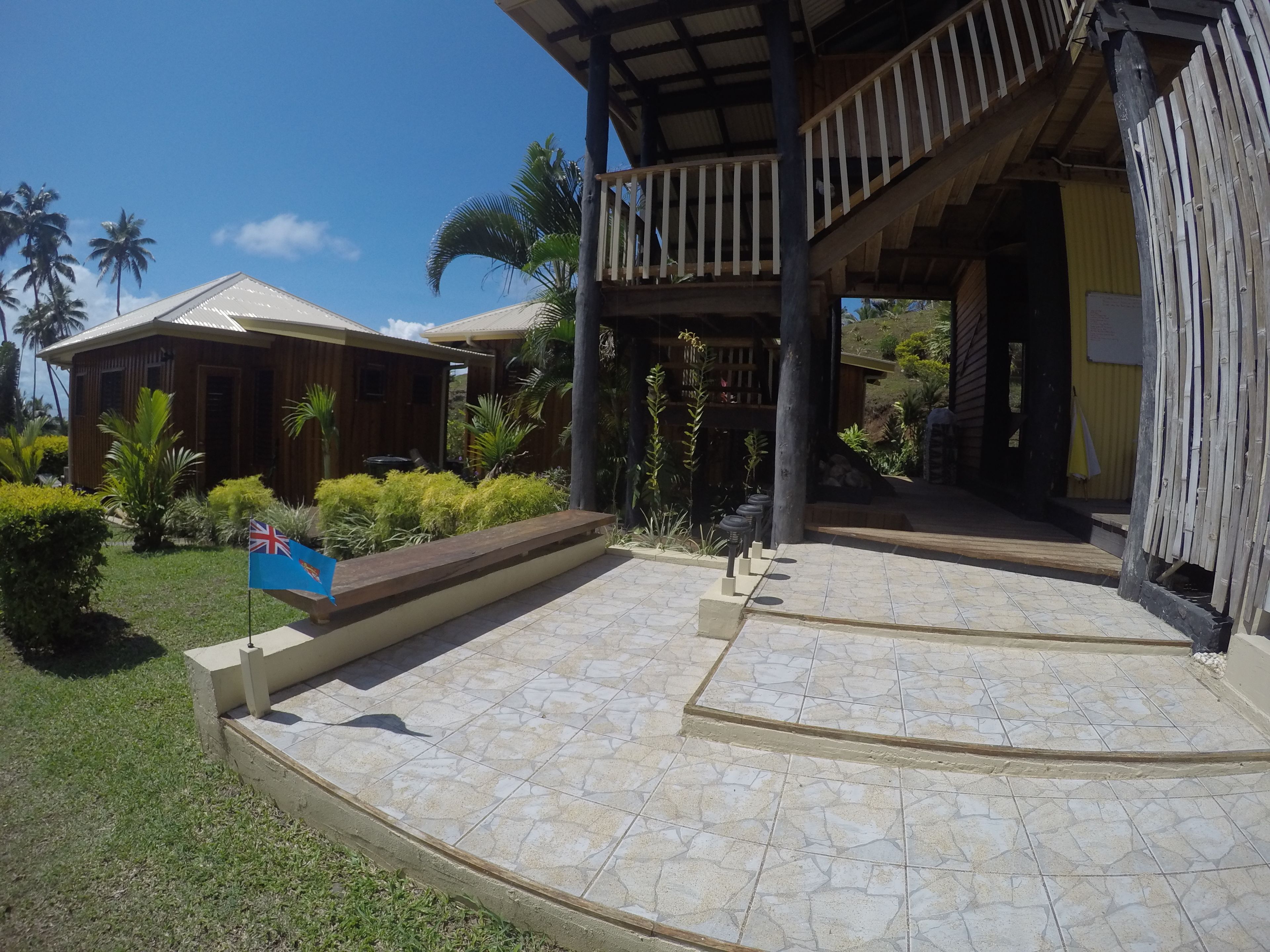 A resort with a covered outdoor area, a flag, and tropical landscaping.