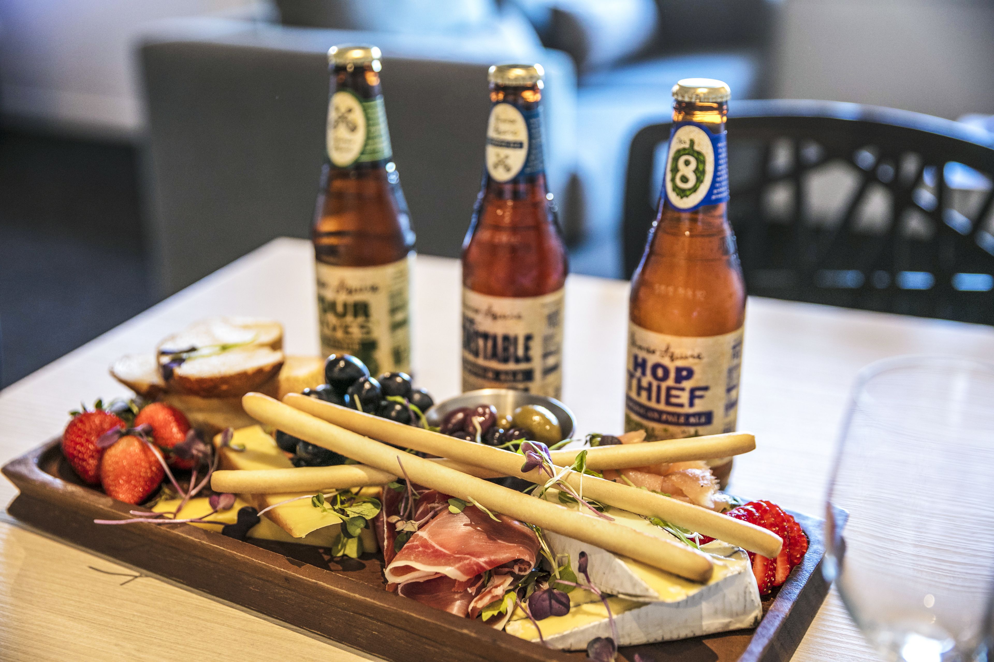 Tábua de frios com queijos, embutidos e uvas, acompanhada por três garrafas de cerveja.