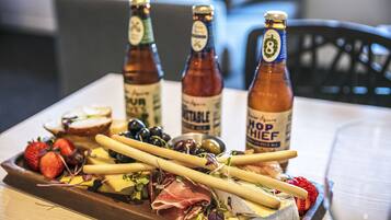 Tábua de frios com queijos, embutidos e uvas, acompanhada por três garrafas de cerveja.