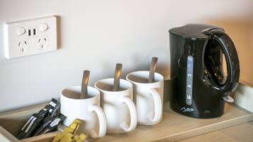 Una bandeja de madera con tazas blancas, una cafetera negra y sobres de leche para café.
