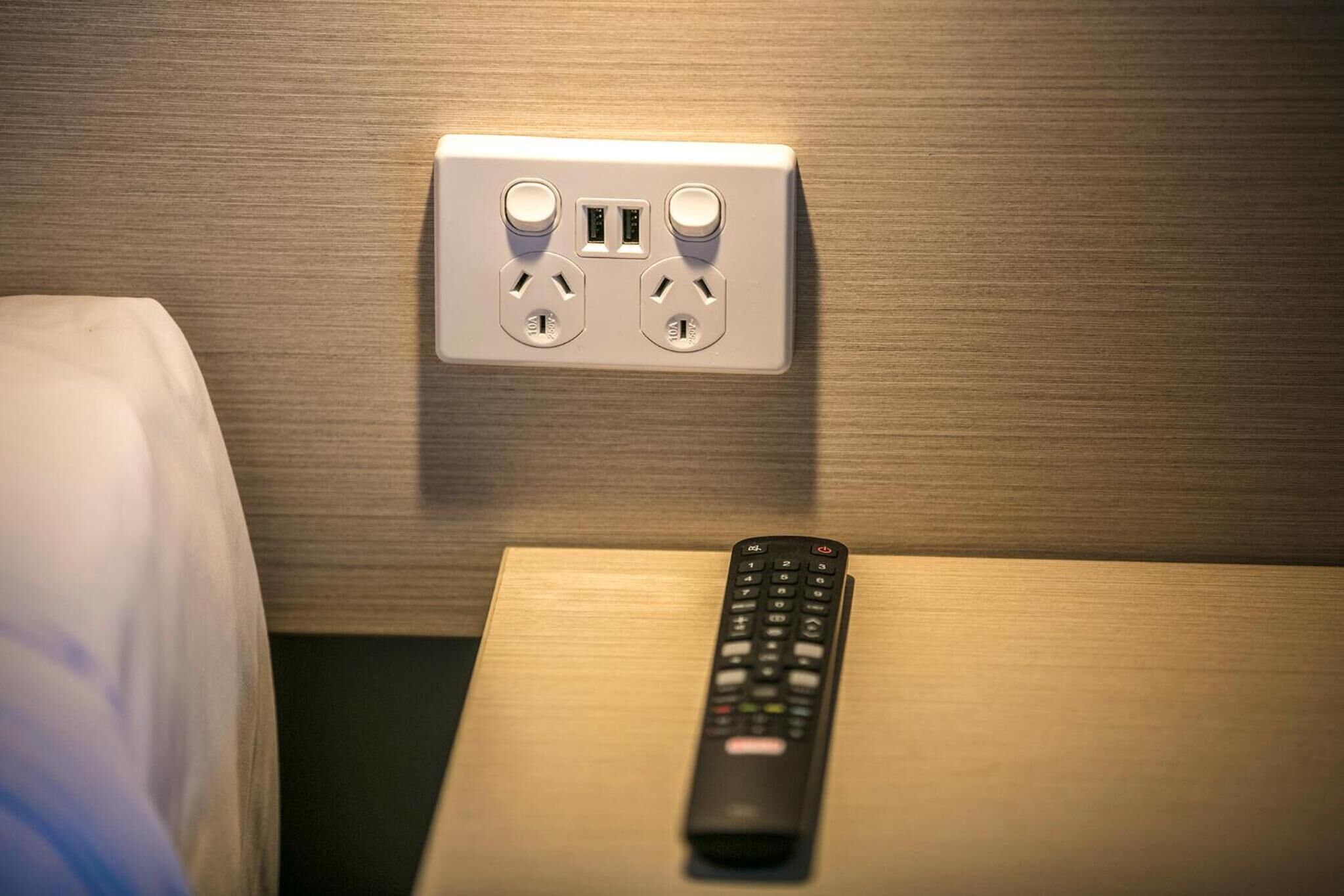 A bed with a remote control on a wooden nightstand.