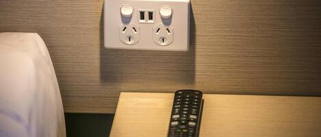 A bed with a remote control on a wooden nightstand.