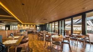 Ein geräumiges Restaurant mit Holzboden, hohen Decken und großen Fenstern, die einen Blick ins Freie bieten.