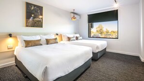 Ein Hotelzimmer mit zwei Betten, einem großen Fenster mit Blick auf die Stadt, einer Deckenleuchte und einer Wand-Klimaanlage.