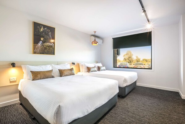 A hotel room with two beds, a large window with a city view, a ceiling light, and a wall-mounted air conditioner. - Nightcap at The Cheeky Squire (Frankston)