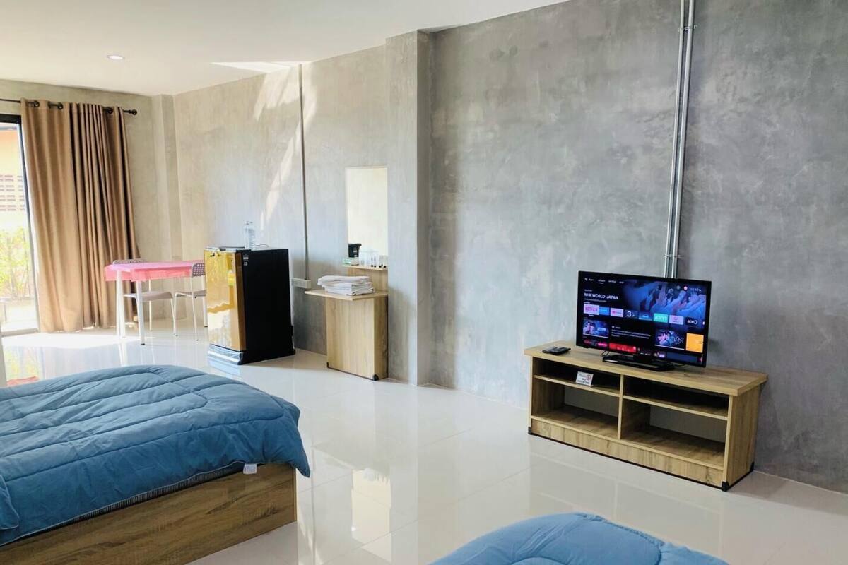 A modern hotel room with a bed, a TV, a desk, and a refrigerator.