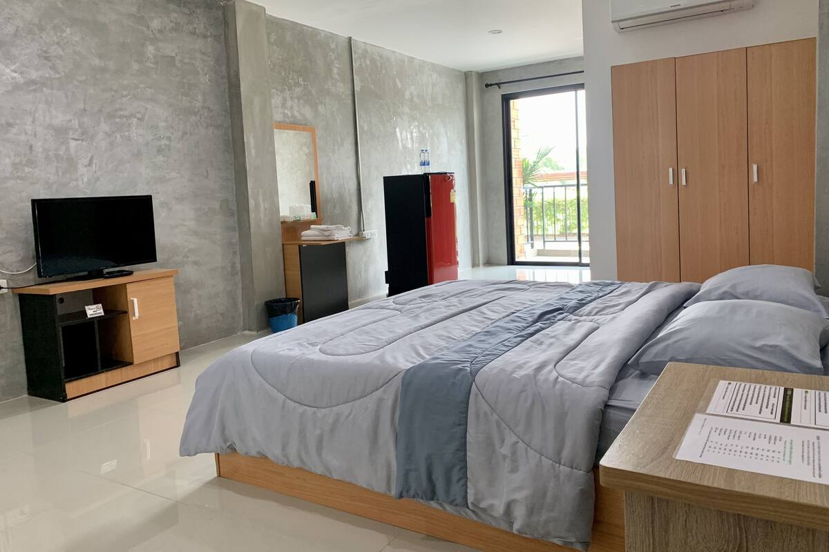 A modern bedroom with a bed, a TV on a wooden stand, a wardrobe, and a balcony with a view.