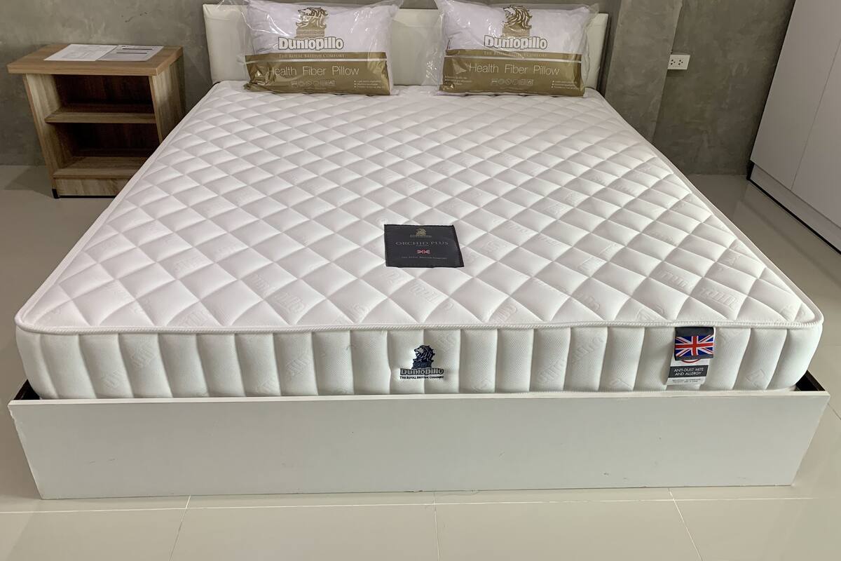 A bed with a quilted mattress, two pillows, and a bedside table with paperwork.