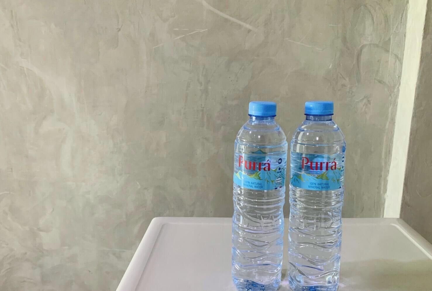 Dos botellas de agua mineral Pura sobre una superficie blanca frente a una pared con textura.