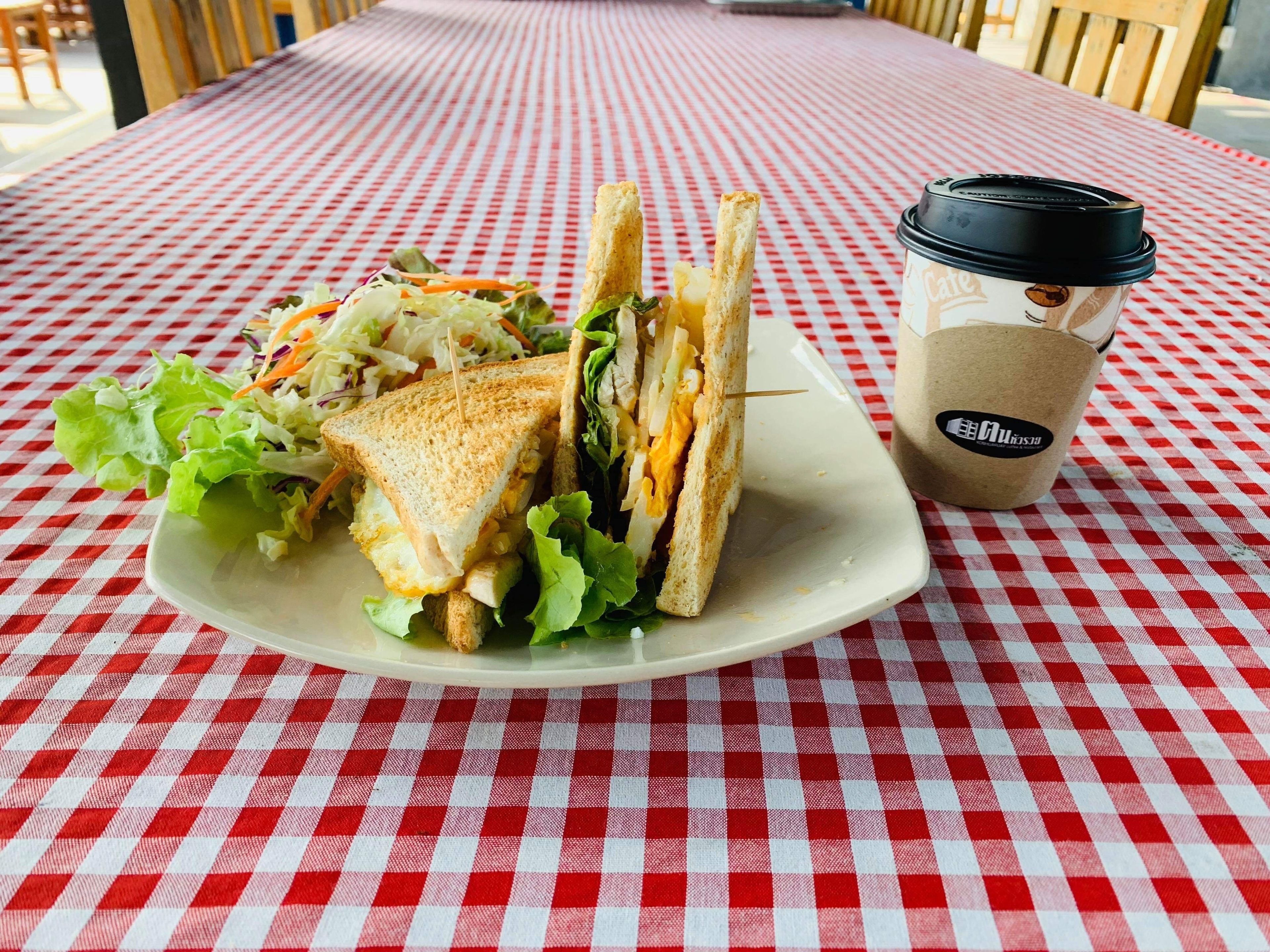 A sandwich on a white plate with a side salad and a coffee cup on a red and white checkered tablecloth.
