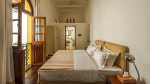 A bedroom with a bed, a nightstand, a mirror, and a view of a bathroom through an open door. - Mateus Boutique Hotel (Panaji)