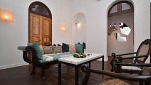 A cozy room with a wooden bench, a table, and a chair. There are two arched doorways and wall-mounted lights. - Mateus Boutique Hotel (Panaji)