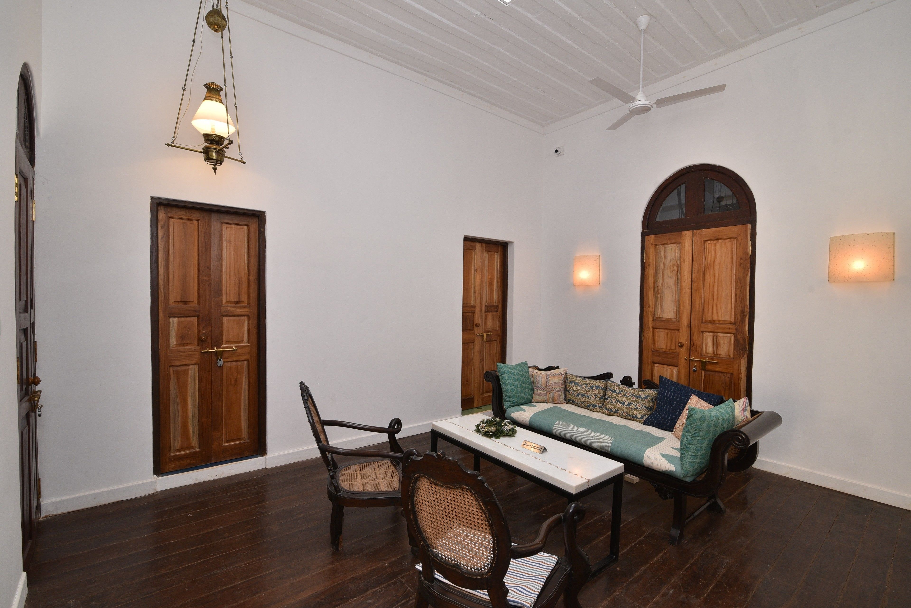 Um quarto com piso de madeira, uma mesa de jantar com cadeiras, um sofá com almofadas e duas portas de madeira.