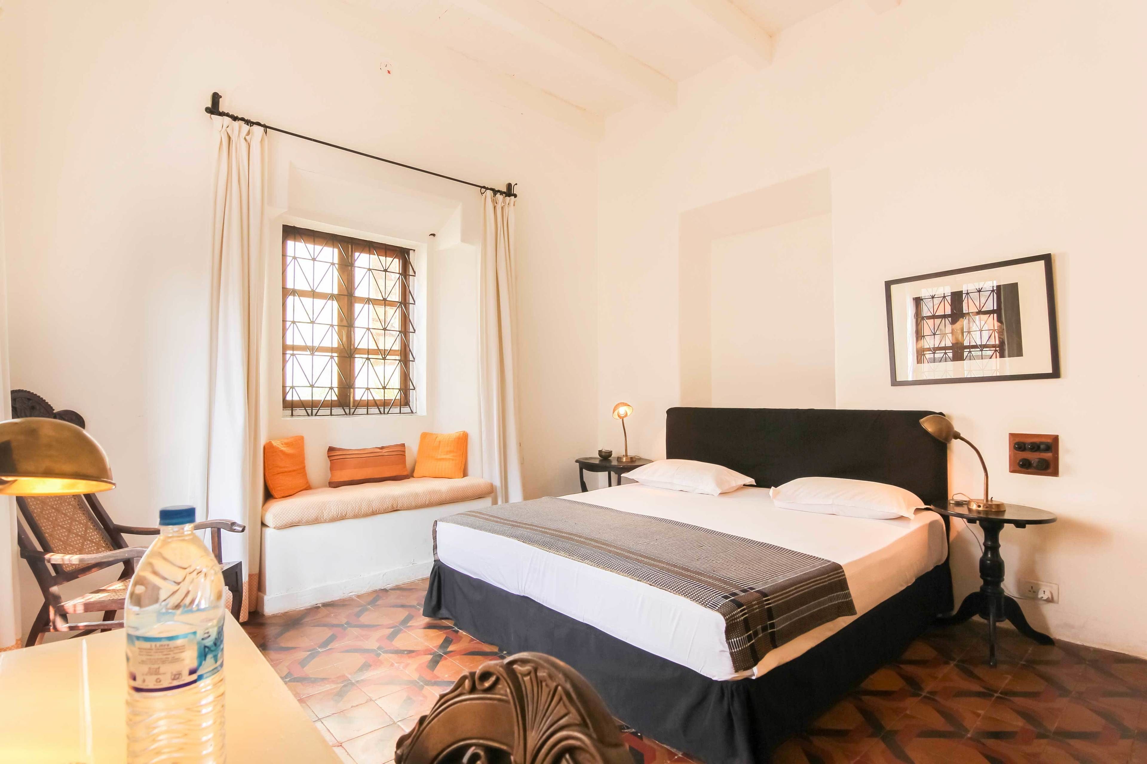 Habitación de hotel con cama, ventana con cortinas, escritorio con lámpara y una botella de agua.