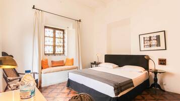 Habitación de hotel con cama, ventana con cortinas, escritorio con lámpara y una botella de agua.